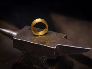 An image of a gold ring sitting upright on small iron anvil.